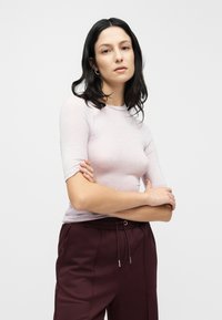 Ανοιχτό μωβ εφαρμοστό τοπ με κοντά μανίκια, ριμπ γιακά και μαλακή υφή, συνδυασμένο με παντελόνι με ελαστική ζώνη σε σκούρο βουργουνδί χρώμα.