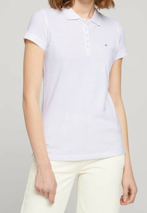 Wit katoenen poloshirt met een kraag, een knoopsluiting met zeven knopen en korte mouwen. Heeft een klein logo op de linkerborst. Gladde textuur.