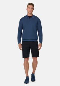 Blå pullover med kvartlynlås og krave, kombineret med sorte shorts og blå træningssko. Glat stoftekstur; afslappet design.