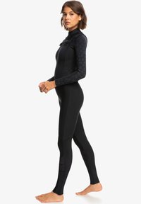 Black wetsuit featuring long sleeves, a high neck, and textured long sleeves with a subtle pattern. Designed for water activities, it fits closely.
