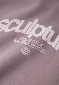 Ljubičasta tkanina sa velikim bijelim tekstom koji glasi "sculpture COLLECTIVE APPAREL EDITION" uz ikonu globusa. Vidljiva teksturirana površina.