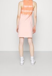 Vestido tipo tanque en durazno claro con efecto de tie-dye en la parte posterior. Tejido de algodón suave, corte recto, hasta la rodilla. Combinado con zapatillas altas blancas.