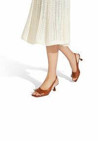 Brune, læder slingback-sko med firkantet tå, sløjfedetalje og en lille hæl, parret med en lys, tekstureret striknederdel.
