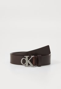 Hnedý kožený opasok s hladkou textúrou. Má striebornú kovovú pracku s logom "ck". Konce sa zaostrujú, čo zdôrazňuje minimalistický dizajn.