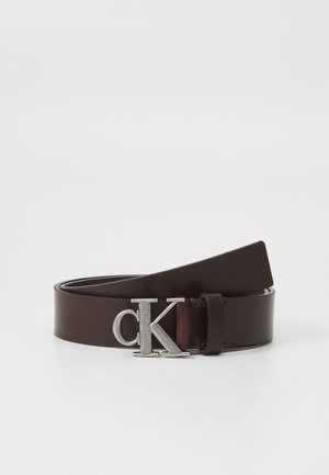 Cintura in pelle marrone con una texture liscia. Presenta una fibbia in metallo argentato con logo "ck". Le estremità si assottigliano, mostrando un design minimalista.