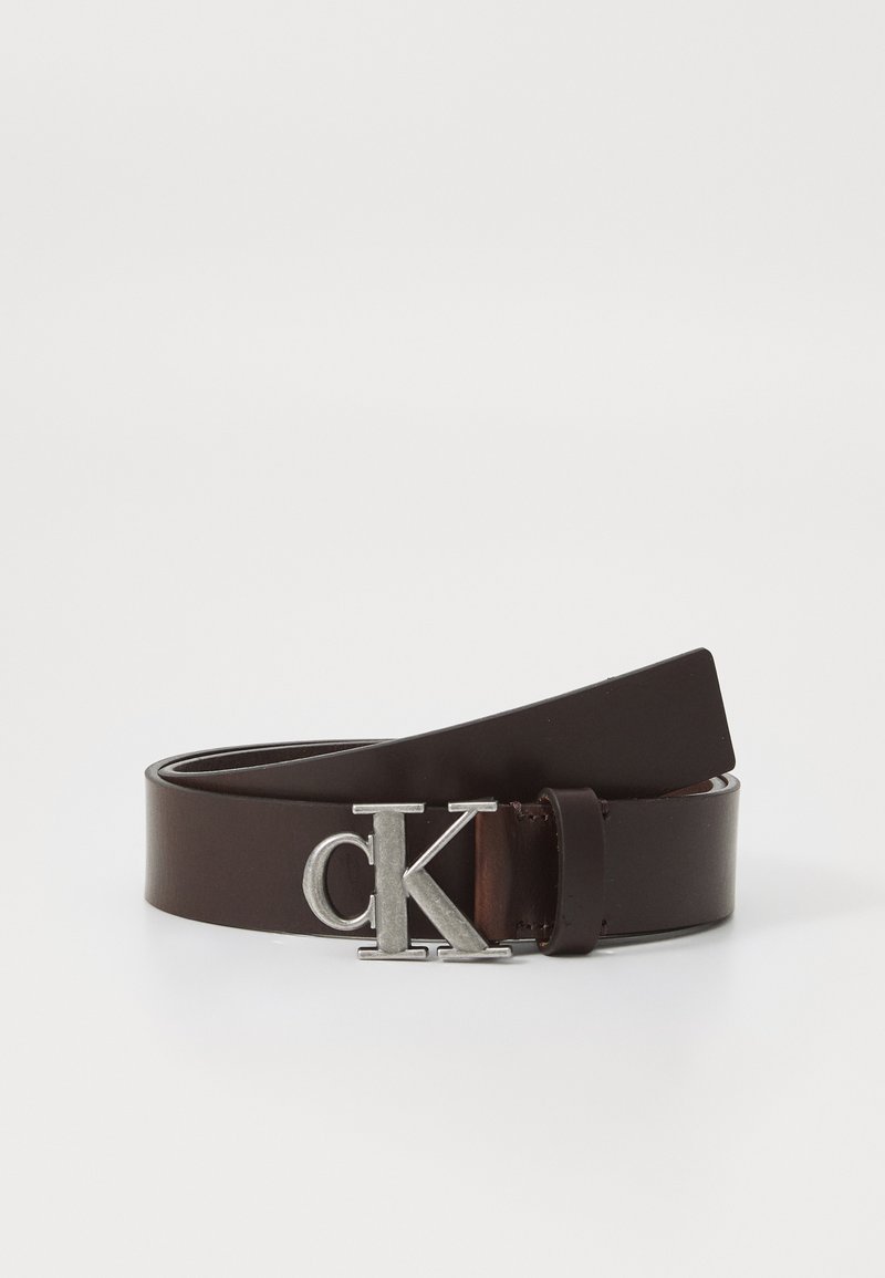 Hnedý kožený opasok s hladkou textúrou. Má striebornú kovovú pracku s logom "ck". Konce sa zaostrujú, čo zdôrazňuje minimalistický dizajn.