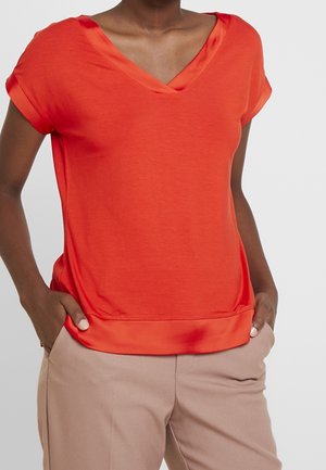 Haut rouge à col en V avec manches courtes, orné d'un bord en satin et de coupe décontractée, associé à un pantalon marron clair. Texture de tissu lisse.