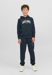 Conjunto de sudadera con capucha y pantalones de chándal en azul marino, con el logo blanco de "JACK & JONES" y detalles a juego en los pantalones. Material de algodón suave.
