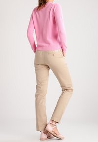 Ljusrosa stickad tröja, beige slim-fit byxor och blekrosa sandaletter med remmar. Anmärkningsvärda egenskaper: texturerad tyg och vristremmar.