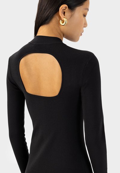 Robe noire à manches longues et à côtes, avec une grande découpe dans le dos et une texture lisse, présentant un design ajusté. Boucles d'oreilles en or visibles.