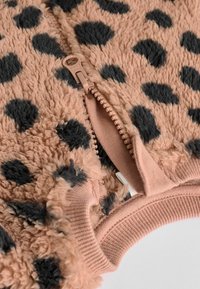 Giacca in pile con zip di colore rosa chiaro, caratterizzata da una superficie morbida e testurizzata con pois neri. Include una zip robusta e polsini a costine.