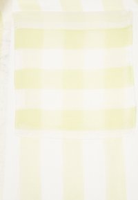 Tessuto bianco con strisce verticali giallo chiaro, dotato di una tasca a toppa. Il materiale appare leggero e leggermente trasparente.