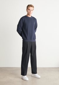 Marinblå sweatshirt med rund hals, matchad med svarta byxor och vita sneakers. Slät tyg, minimalistisk design och en liten logotyp på bröstet.