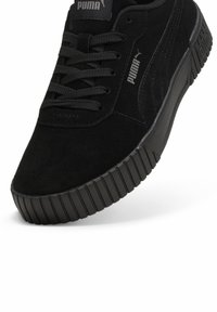 Schwarze Wildledersneaker mit strukturiertem Gummisohle, ausgestattet mit schwarzen Schnürsenkeln, einem Logo auf der Zunge und minimalen Akzenten an den Seiten.
