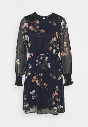 Robe noire à imprimé floral avec des manches longues, taille élastique et tissu transparent. Présente des motifs de fleurs roses et blanches. Associée à des bottes noires montantes.