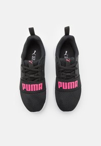 Chaussures de sport noires avec un dessus en maille, marquage "PUMA" rose au niveau du cou-de-pied, fermeture à lacets et semelles blanches.