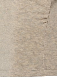 Hellbeige Oberteil mit einem weichen, strukturierten Strickstoff, der subtile tonale Variationen aufweist, und einem gerafften Detail an der Seitennaht.