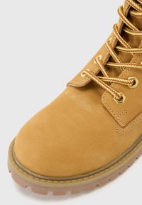 Bottine en suède beige avec des œillets en or et des lacets tressés jaunes. Bout rond et semelle en caoutchouc avec un motif texturé.
