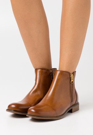 Hnědé kožené kotníkové boty s oblým špičkou, bočními zipy a nízkým stočeným podpatkem. Hladká textura s jemnými švy.
