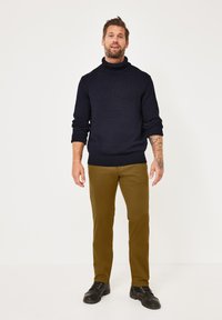 Navy knit turtleneck sweater, olive-green trousers, and black lace-up boots. Sweater features ribbed cuffs and hem.