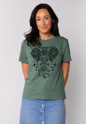 Groene katoenen t-shirt met een zwart olifantgrafiek en ingewikkelde ontwerpen, met de tekst "WEES STERK" eronder. Klassieke ronde hals en korte mouwen.