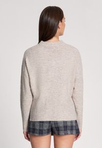 Beżowy sweter dzianinowy z ribbowym wykończeniem u dołu i okrągłym dekoltem, charakteryzujący się luźnym krojem i opadającymi ramionami, widoczny z tyłu.