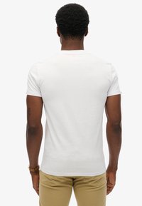 Biała koszulka z krótkim rękawem, wykonana z bawełny, z klasycznym okrągłym dekoltem i gładką fakturą. Brak widocznych logosów lub wzorów.