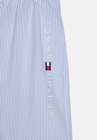 Modrá a biela pruhovaná tkanina s elastickým pásom; obsahuje vyšívaný text "TOMMY HILFIGER" a malý detail vlajky v červenej, bielej a modrej farbe.