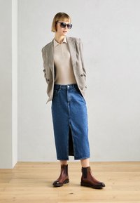Brūni ādas potīšu zābaki, džinsu svārki ar priekšēju šķēlumu, bēšs tops un houndstooth stila žakete. Aksesuāri ietver tumšas saulesbrilles.