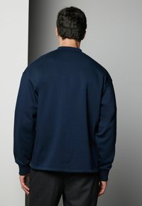 Hanorac bleu marin realizat dintr-un material moale, cu guler rotund, umeri lăsați și manșete ribbate. Design minimalist, fără embellishement.