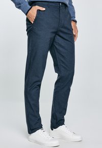 Pantalones azul marino de un tejido texturizado, con bolsillos laterales y cierre de botón, combinados con zapatillas blancas.