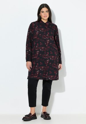 Schwarze Tunika mit rotem Blumenmuster, langen Ärmeln, Knopfverschluss vorne und Kragen; kombiniert mit schwarzen Slim-Fit-Hosen und dunklen Schuhen.
