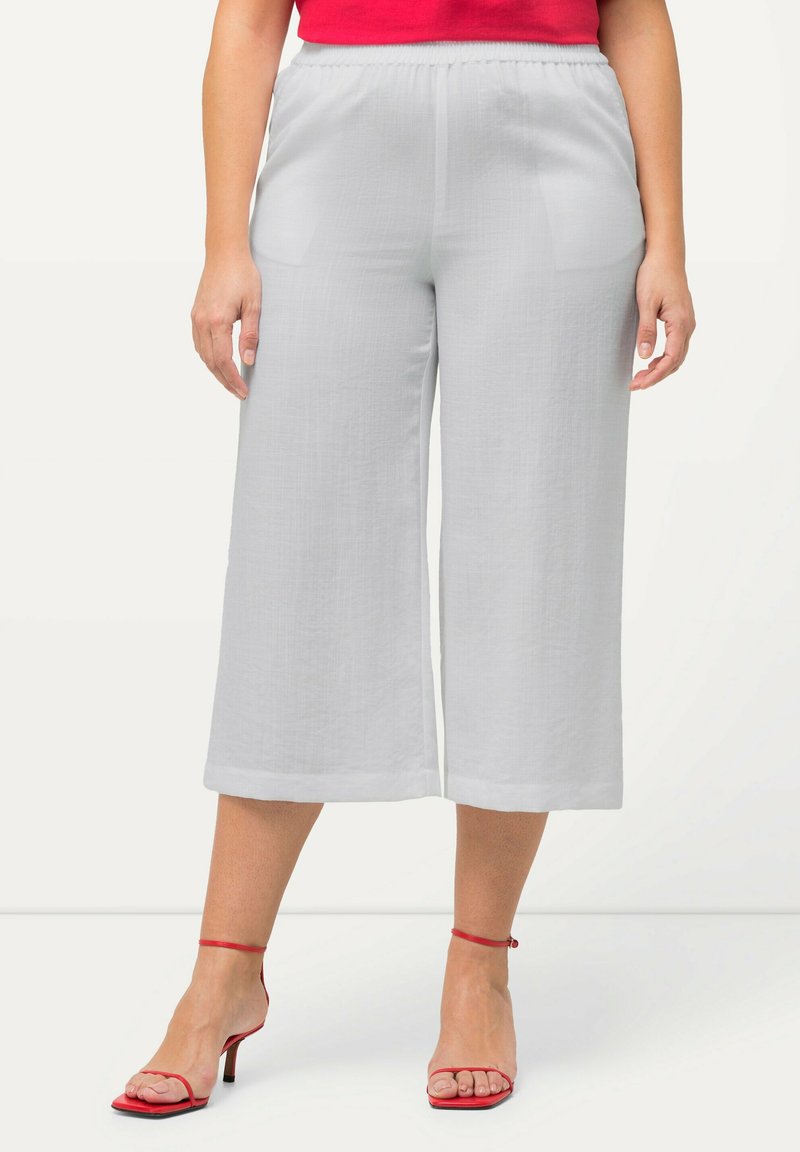 Lichtgrijze wijde broek met een gestructureerde afwerking en elastische tailleband, voorzien van zijzakken, gecombineerd met rode sandaaltjes met bandjes.