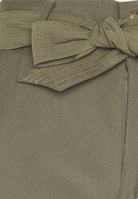 Kalhoty z olivově zelené látky v pase s uzlovým páskem. Mají texturovaný povrch a kontrastní švy podél švů.