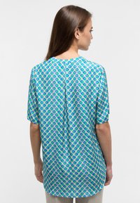 Short-sleeve blouse in green and blue hexagonal pattern, featuring a lightweight fabric and a round neckline with a back seam detail.