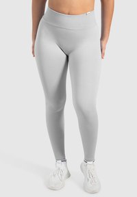Leggings gris clair avec une taille haute, texture lisse et design ajusté. Portés avec des chaussures de sport blanches.