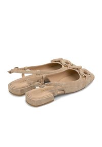 Ballerine slingback in suede beige con punta affusolata, tacco a blocco e dettaglio a fiocco decorativo. Presenta una cinghia alla caviglia con chiusura a fibbia. Finitura strutturata.
