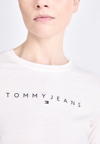Bijela pamučna majica s printom "TOMMYJEANS" u crnoj boji, s malim obojenim logotipom u crvenoj, bijeloj i plavoj. Okrugli izrez.
