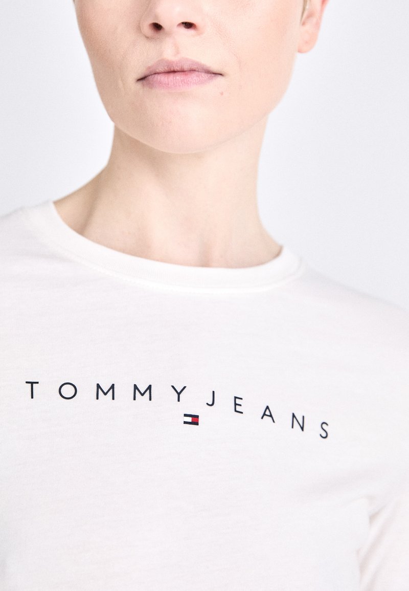 Biała bawełniana koszulka z krótkim rękawem z napisem "TOMMYJEANS" w kolorze czarnym, z małym kolorowym akcentem logo w kolorach czerwonym, białym i niebieskim. Okrągły dekolt.