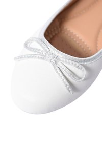 Ballet flat bianco realizzato in pelle liscia. Presenta una punta arrotondata e un elegante fiocco strutturato in argento sul davanti. L'interno è foderato in tonalità beige.
