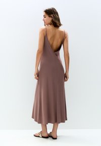 Mauve bezrękawna sukienka z głębokim dekoltem w kształcie V, zwiewna sylwetka i gładki materiał. Stylizowana z płaskimi sandałami i minimalistycznymi akcesoriami.