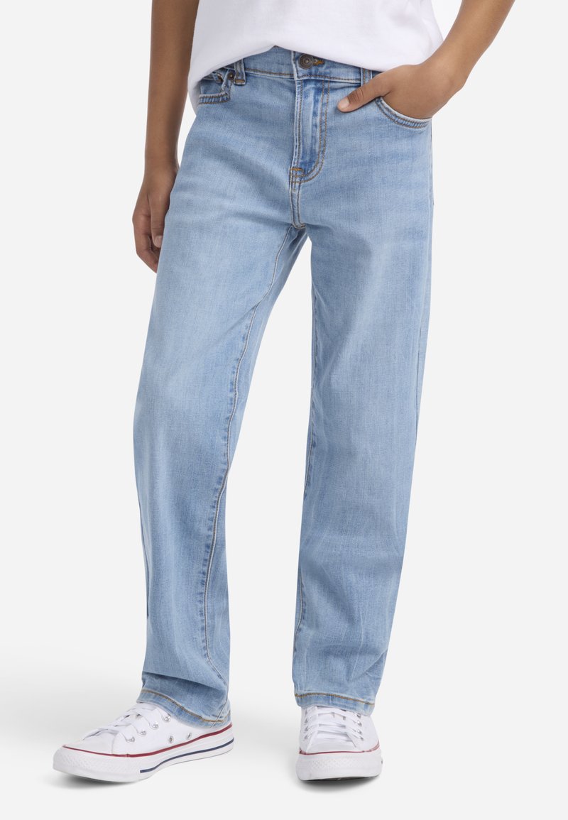 Jasnoniebieskie dżinsy o prostym kroju, z pięcioma kieszeniami i widocznym przeszyciem. W połączeniu z białymi trampkami.