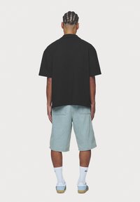 Maglietta nera a maniche corte con una finitura strutturata, abbinata a pantaloncini di jeans azzurri. Calzini bianchi al polpaccio e sneakers azzurre completano il look.