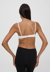 Reggiseno bianco con spalline sottili regolabili e chiusura a gancio sul retro. Tessuto liscio con un design semplice.