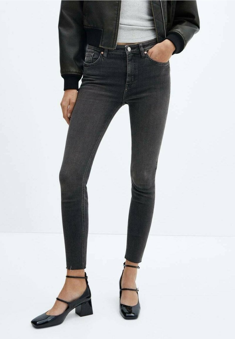 Jeans ajustados en denim gris oscuro, con una cintura alta, diseño clásico de cinco bolsillos y dobladillos deshilachados. Combinados con zapatos negros de tacón cuadrado.