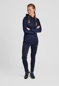 Felpa sportiva navy con tasca frontale e pantaloni abbinati, entrambi in un tessuto morbido; presenta dettagli con logo sul petto e sulla gamba.
