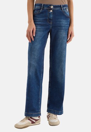 Brede jeans van denim in het blauw. Heeft een sluiting met twee knopen, voorzakken en zichtbare stiksels. Gecombineerd met beige en burgundy sneakers.