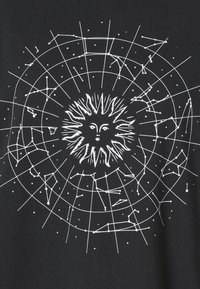 Camisa negra con un motivo de sol blanco en el centro, rodeado de patrones de constelaciones y un diseño de cuadrícula circular.