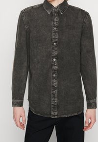 Svart denimskjorta med knapp-ner krage, framknappar och en subtil logobrodyr. Lätt sliten textur och rundad nederdel.