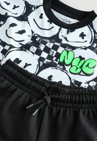 Shorts noirs avec taille élastique et cordon de serrage, associés à un haut blanc orné de visages souriants noirs et d'un accent de texte "NYC" vert.